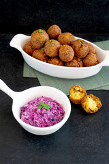 Traditional Middle Eastern food, Falafel (tamiya) with  red cabbage salad with vegan mayonnaise on black wooden background and green table cloth. Selective focus some areas are blurred. 