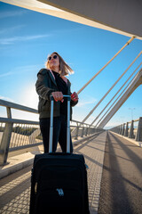 Mujer de negocios viajando con maleta en un puente exterior gafas de sol rubia con chaqueta invierno