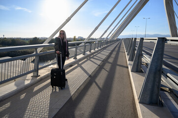 Mujer de negocios viajando con maleta en un puente exterior gafas de sol rubia con chaqueta invierno