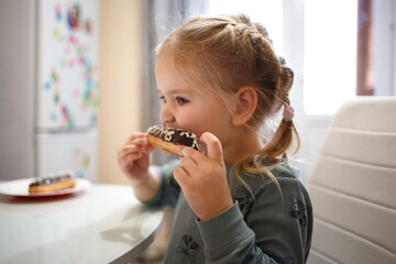 little cute girl eating cake while sitting at the kitchen table