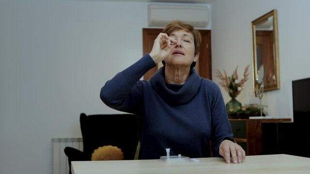Senior woman sitting at home introducing the nasal swab to the buffer tube after taking a nasal culture sampling from her nose. Self testing Rapid Antigen Test for Covid-19, Coronavirus. Tracking shot