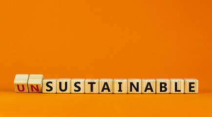 Sustainable or unsustainable symbol. Turned a cube and changed word 'unsustainable' to 'sustainable' on wooden cubes. Beautiful orange background, copy space. Business and sustainable concept.