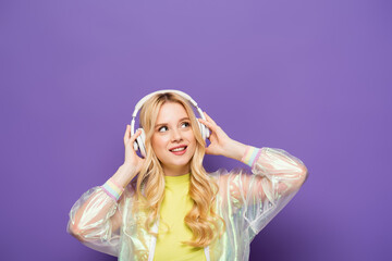 happy blonde young woman in colorful outfit and headphones on purple background.