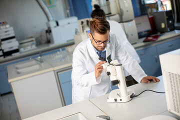 Fototapeta na wymiar Young scientist in white lab coat working with binocular microscope in the material science lab