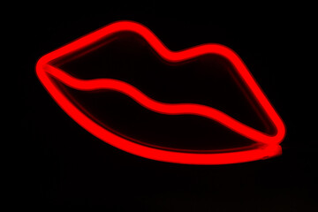 Blurry neon red lips close-up on a black isolated background.