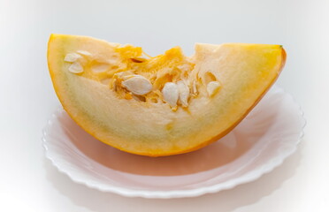 A piece of pumpkin in close-up on a white ceramic plate on a white background. Focus in the center