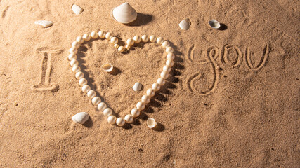 Shells and pearl necklace on the beach sand with romantic phrases written in the sand, selective focus.