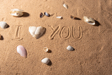 Fototapeta na wymiar Shells on the beach sand with romantic phrases written in the sand, selective focus.
