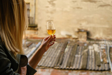 Beautiful girl with a wine glass on the balcony. Drinks white wine and enjoy the moment. A celebration holiday alone. Relaxed lifestyle. Happy woman rest after work. Beautiful European courtyard