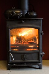 Close up of a log burner glowing with a kettle and potato baker on the top - 401248113