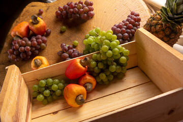 Grapes in a wooden box and cashews and pineapple with fabrics in the background and rustic wood, low depth of field, selective focus.