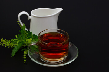 Holy Basil or tulsi tea in transparent glass cup and holy basil leaf on black background. Popular ayurvedic medicine in India  