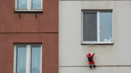 Fototapeta na wymiar Toy Santa Claus climbing on the wall. Santa Clause figure hanging on rope from a window of house. Christmas and Happy new year background.