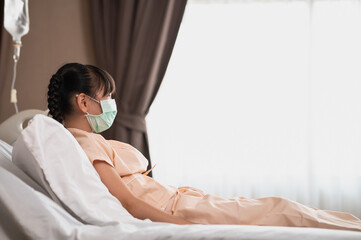 Recovering Asian girl wear surgical mask and sitting on hospital bed feeling sad and unhappy....