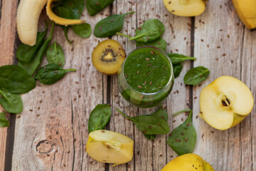 
A glass of kiwi, spinach and apple smoothie. Health drink. Apples, flax seeds, spinach, kiwi, bananas lie nearby.