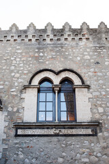Detail of the stonewall with a window and merlons of the Palace Corvaja in Taormina, Sicily, Italy.  