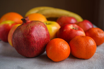 Fresh fruit lies on a gray canvas, in the foreground pomegranate and tangerine, side view