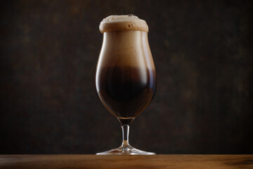 Glass of Dark beer with overflowing foam head.