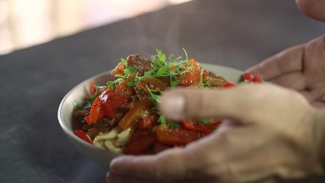 The cook puts on the table a plate of steaming food with pasta and vegetables