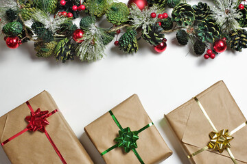 New Year or Christmas gifts presents in craft paper with metallic red, yellow and green bows and ribbons on white background. Garland from frosty pine branches, cones, red balls and berries.