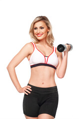 Portrait of a fit, young white female athlete with curly long blond hair posing by herself holding a dumbbell in a studio with white background wearing black shorts & sports bra.