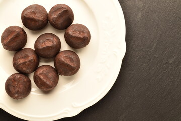 Several delicious chocolate truffles on a white ceramic dish, close-up, on a slate board.
