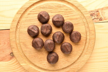 Several delicious chocolate truffles on a round wooden tray, close-up, on a wooden table.