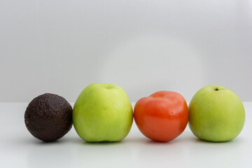 A red tomato , an avacado placed next to  green apples  showcasing diversity and friendship with white back ground