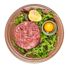 top view of Steak tartare (raw minced beef meat) and yolk in bowl on fresh greens on brown plate isolated on white background