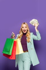 happy blonde young woman in fashionable turquoise blazer with shopping bags and money on purple background.