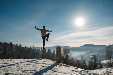 Man practicing yoga and balancing exercises in the winter mountains and enjoying life. Copy, empty...