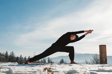 Man practicing yoga and balancing exercises in the winter mountains and enjoying life. Copy, empty...