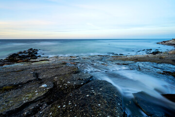 Small river flowing over boulders into the ocean