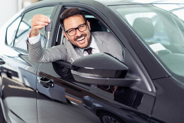 Fototapeta na wymiar Handsome businessman is sitting in a new car in car dealership