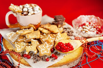 Christmas gingerbread cookies, with fresh berries in a wooden spoon, on a wooden stand and a cup of hot chocolate with marshmallows in the back, on a red background, large depth of field, selective fo