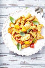 Pasta with chicken breast, cherry tomatoes and fresh basil. Bright wooden background. Top view.