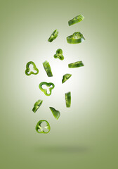 sliced green pepper falling from top to bottom, rings of fresh green pepper flying down on green background