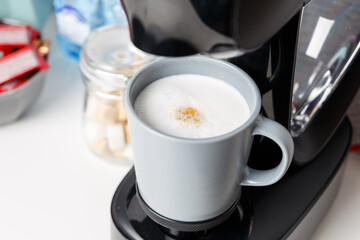 The coffee machine pours cappuccino into the cup. Coffee-make, coffee from the machine at home. Close-up of espresso making from a coffee machine