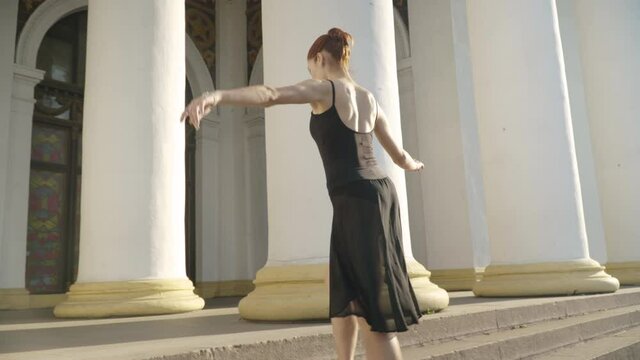 Camera follows slim Caucasian woman in pointes walking up the stairs on tiptoes. Elegant confident ballerina strolling outdoors on sunny summer day. Art and femininity concept.