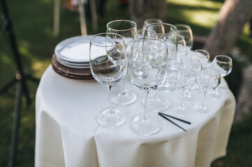 Glass goblets and plates stand on a round white table covered with a tablecloth as decorations for a banquet or buffet table.