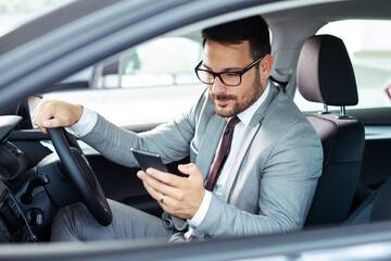 Businessman texting on his mobile phone while driving.