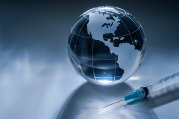 Glass globe and syringe on gray background