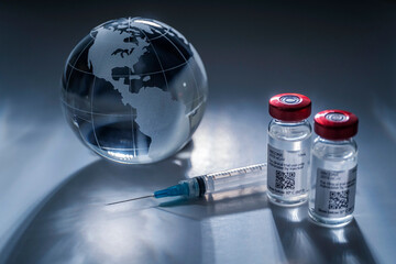 Glass globe and syringe with vaccine on gray background