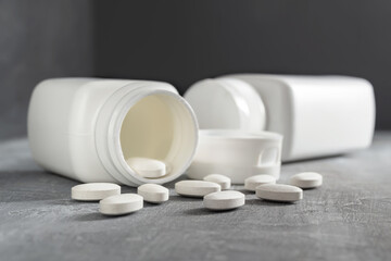 White pills and bottle on textured grey background, medicines, antibiotic, calcium, painkiller,...