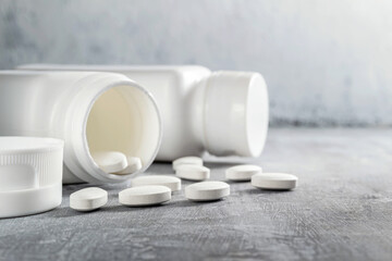 White pills and bottle on textured grey background, medicines, antibiotic, calcium, painkiller, vitamin supplements close-up view