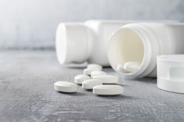 White pills and bottle on textured grey background, medicines, antibiotic, calcium, painkiller, vitamin supplements close-up view