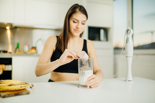 Woman with immersion blender making banana chocolate protein powder milkshake smoothie.Adding a scoop of low carb whey protein mix to shake after a home workout.Diet after the gym.Healthy lifestyle