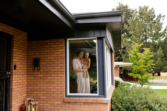 Mother with baby son (18-23 months) standing behind window