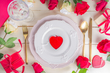 Valentine table setting. Table Dinner place with plates, silverware, champagne wine glass, gift box and roses bouquet top view copy space