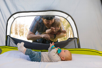 USA, Utah, Uinta National Park, Father and daughter (2-3) peeking into tent and looking at baby boy (6-11 months) inside